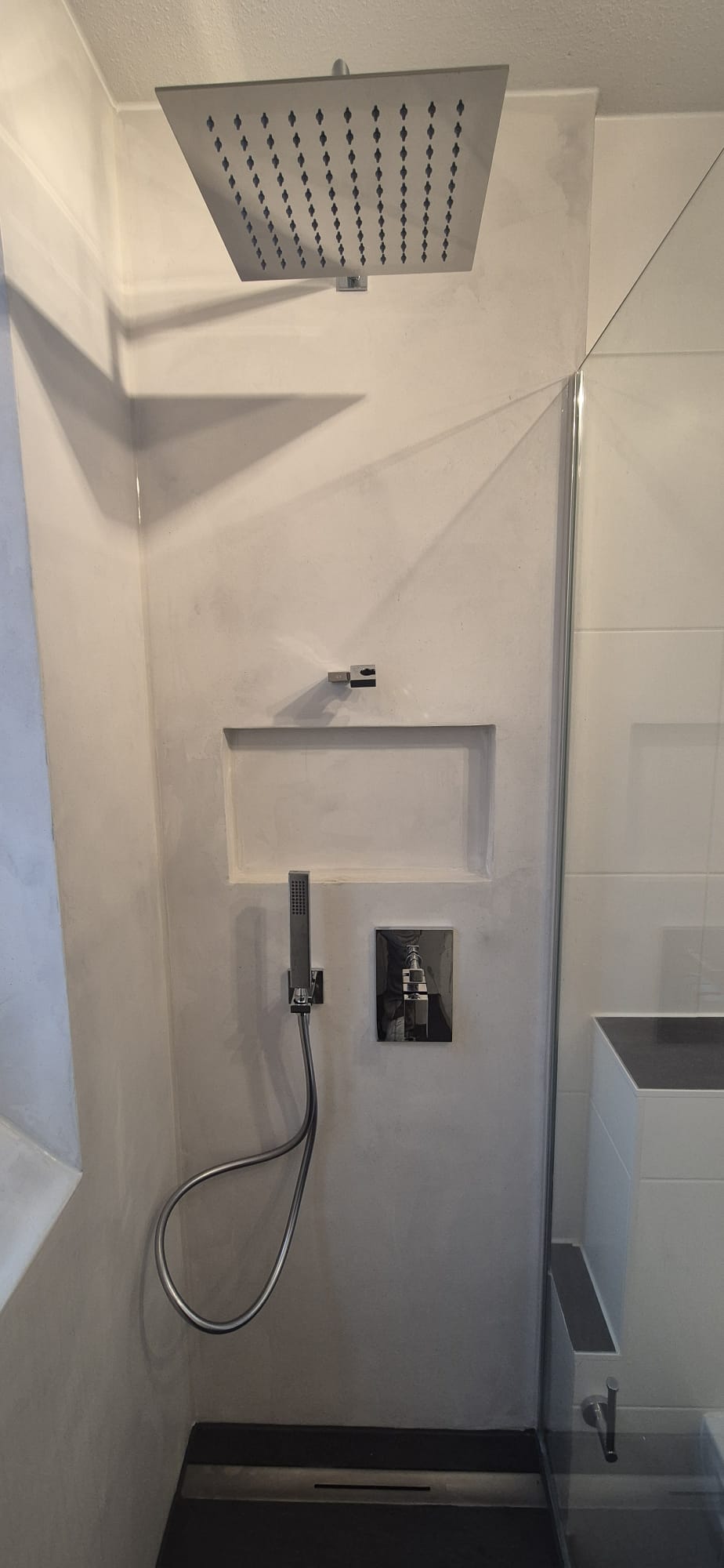 Moderne Regendusche mit Glasabtrennung und integrierter Wandnische in einem sanierten Badezimmer in München