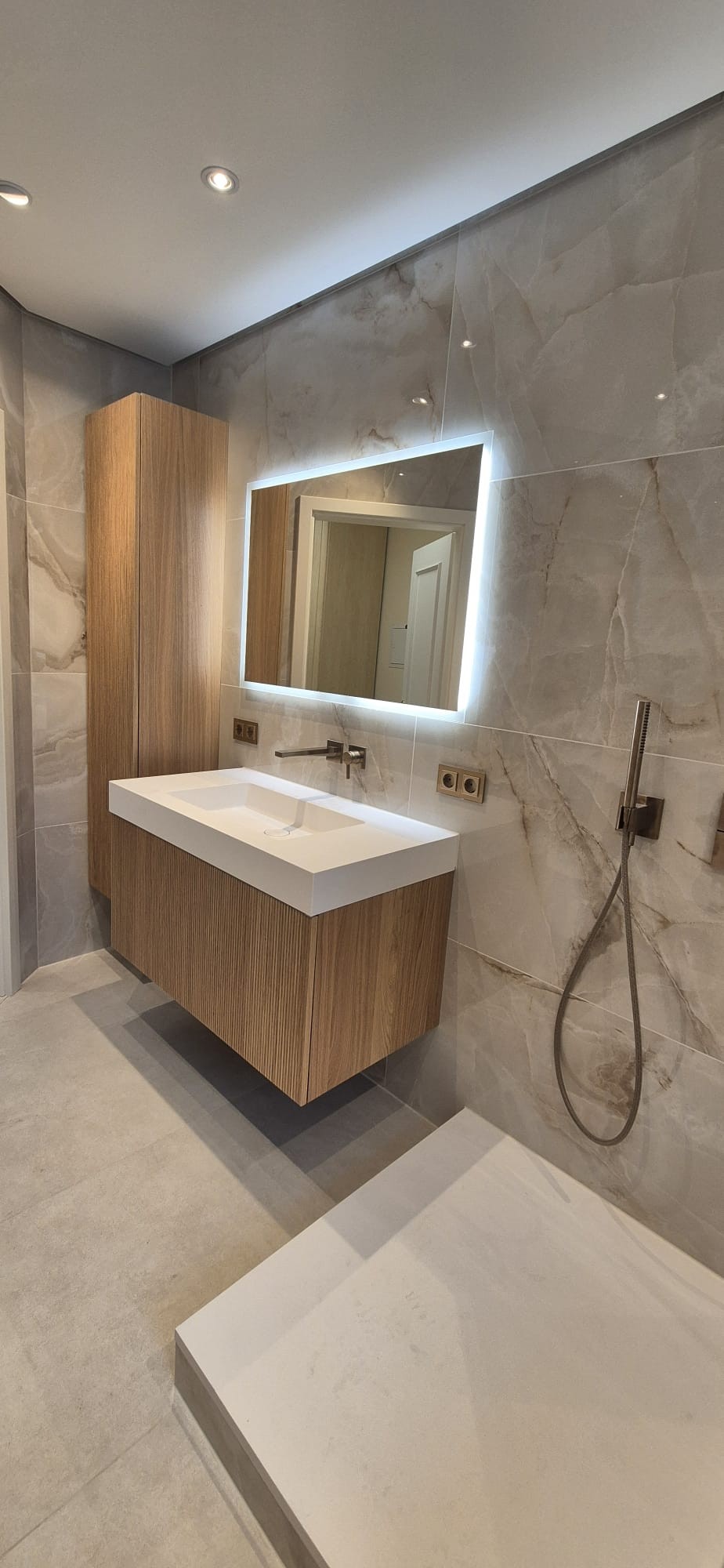 Moderner Waschtisch mit beleuchtetem Spiegel und großformatigen Fliesen in einem sanierten Badezimmer in München