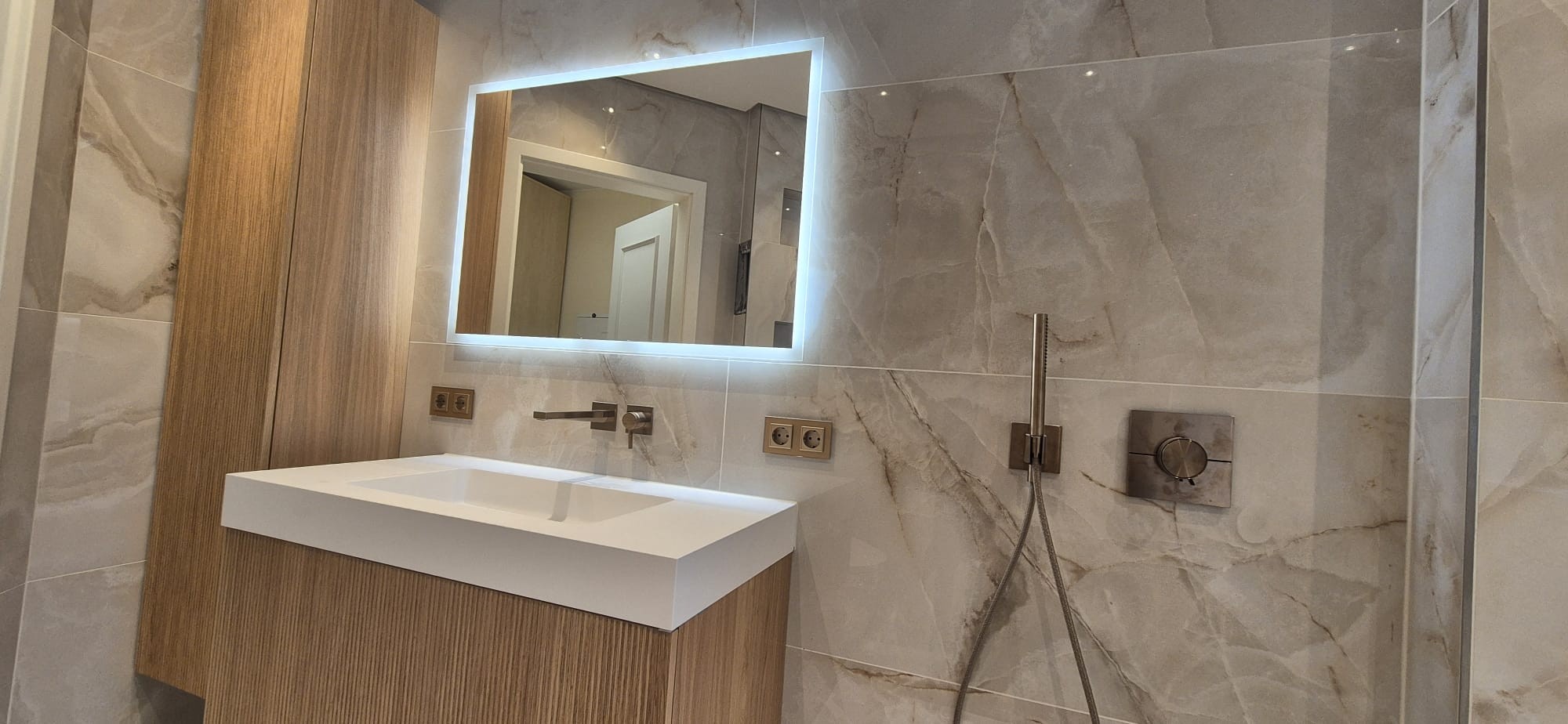 Moderner Waschtisch mit beleuchtetem Spiegel und Duschbereich in einem hochwertig sanierten Badezimmer in München